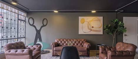 A modern living room with a leather sofa, two armchairs, a black chair, and a large abstract painting on the wall.