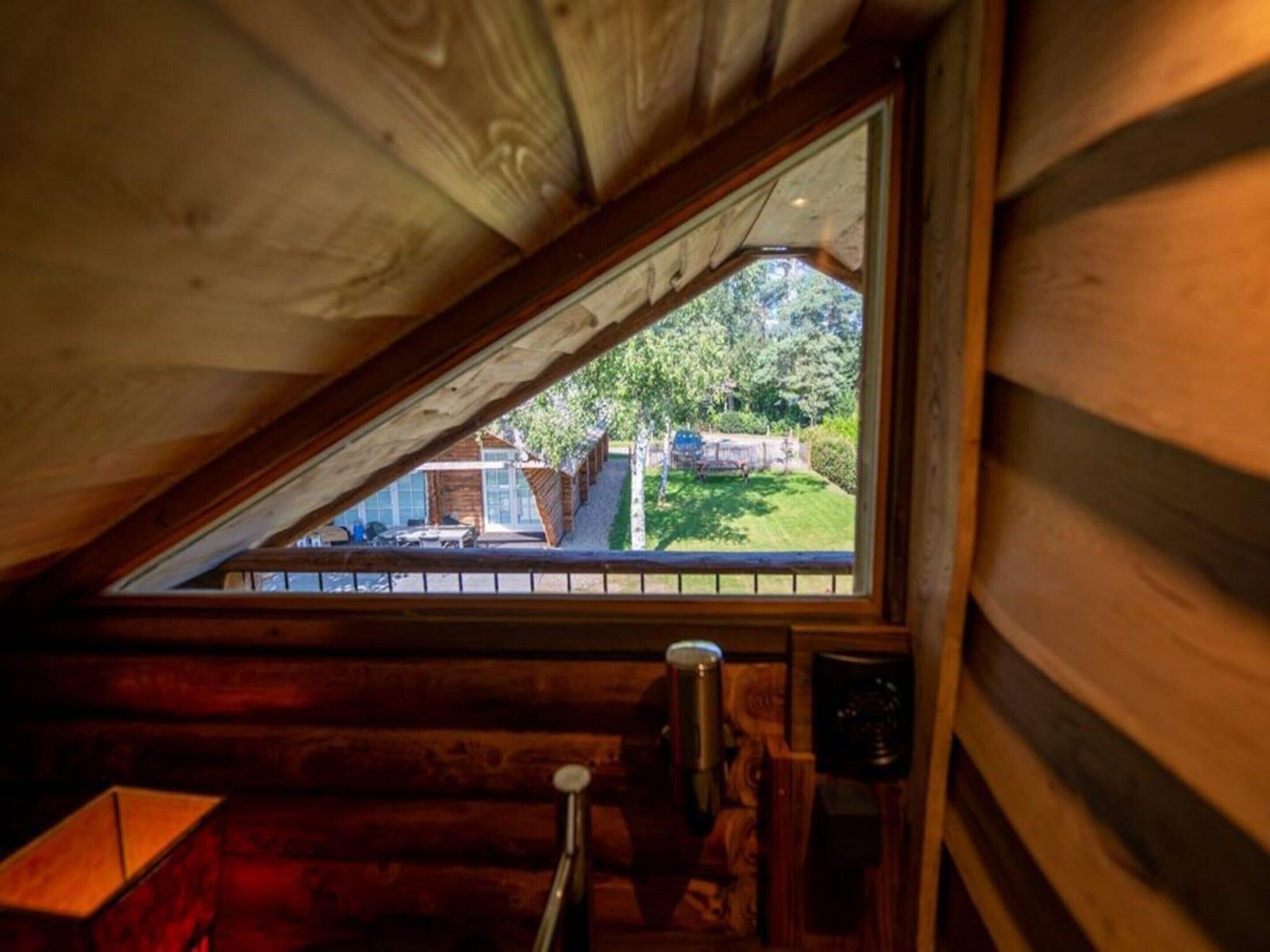 Une chambre de style rustique avec un plafond en pente, une fenêtre donnant sur un jardin, et une table en bois sur laquelle se trouve un récipient en métal.