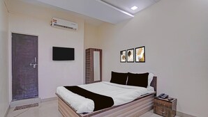 A bedroom with a bed, bedside table, wall-mounted TV, air conditioning unit, and framed artwork. - Collection O Iskcon Aurangabad (Chhatrapati Sambhajinagar)