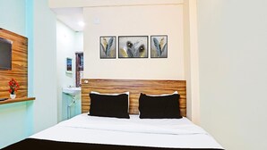 Una habitación de hotel con cabecera de madera, cama con ropa de cama blanco y negro, televisor montado en la pared y tres cuadros de plumas sobre la cama.