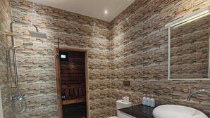 A bathroom with a stone-patterned wall, a white toilet, a white sink, and a shower with a glass door. - Villa Aronora Private Pool & BBQ (Haddada)
