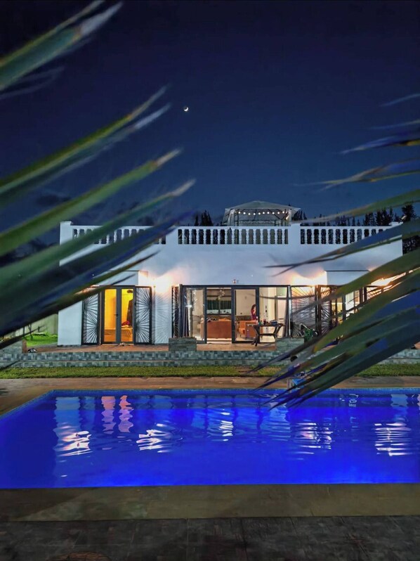 A modern house with a swimming pool, large windows, and a covered outdoor area.