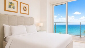 A bed with white linens, a headboard, a nightstand with a lamp, and two framed artworks on the wall. - Luxury Oceanfront Apartment - Playa Escondida 503 (Portobelo)