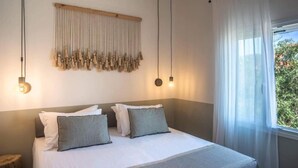 Ein Schlafzimmer mit Bett, Kissen, einer Wandleuchte und einem Fenster mit Vorhängen.