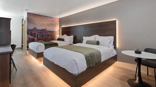 Una habitación de hotel moderna con una cama grande, dos mesitas de noche, una pequeña mesa redonda y un mural en la pared.