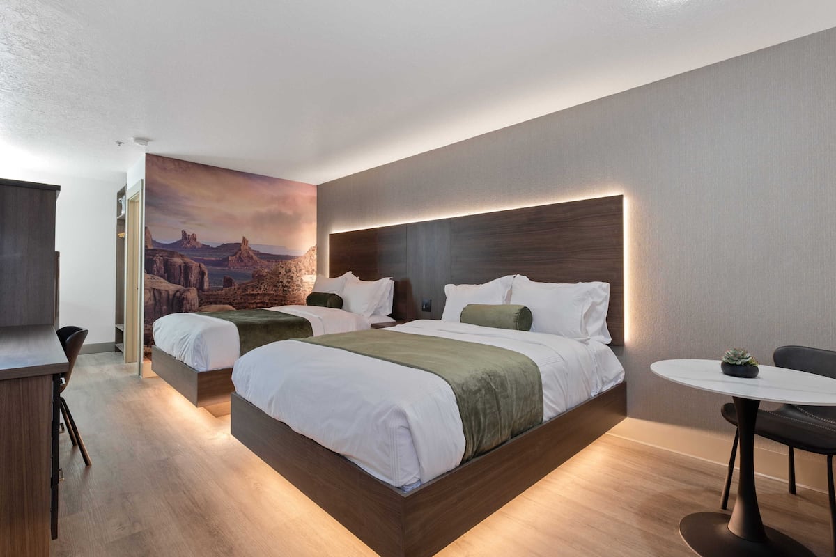 A modern hotel room with a large bed, two bedside tables, a small round table, and a mural on the wall.