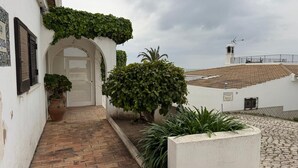 A courtyard with a tiled roof, a white building with a door, and greenery. - TP Maria Luisa dos Olhos Villa - Private Pool and Beach (Olhos de Água)