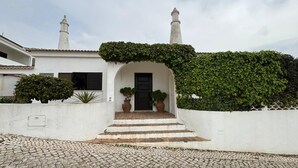 A white building with a black door, steps leading to the entrance, and a white wall with a green ivy-covered section. - TP Maria Luisa dos Olhos Villa - Private Pool and Beach (Olhos de Água)