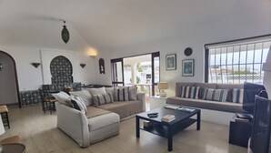 A living room with a sofa, coffee table, and a dining area with chairs. - TP Maria Luisa dos Olhos Villa - Private Pool and Beach (Olhos de Água)