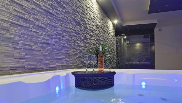 Ein moderner Innenpool mit Steinwand im Hintergrund, einer dekorativen Vase und zwei Gläsern am Rand.