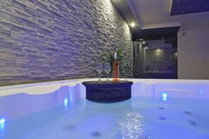 Una piscina interior moderna con un fondo de pared de piedra, un jarrón decorativo y dos vasos en el borde.
