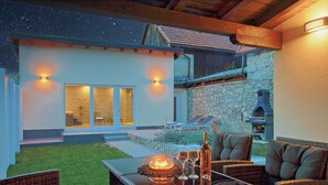 Eine Terrasse mit Korbmöbeln, einem Tisch mit Kerze und Gläsern sowie ein Steinhaus mit Kaminofen.