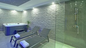 Ein moderner Wellnessraum mit Whirlpool, zwei Liegesesseln und einer in Glas abgeschirmten Duschkabine.