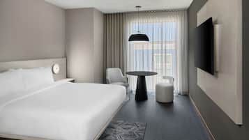 A hotel room with a large bed, a round table, a chair, a TV, and a window with curtains.