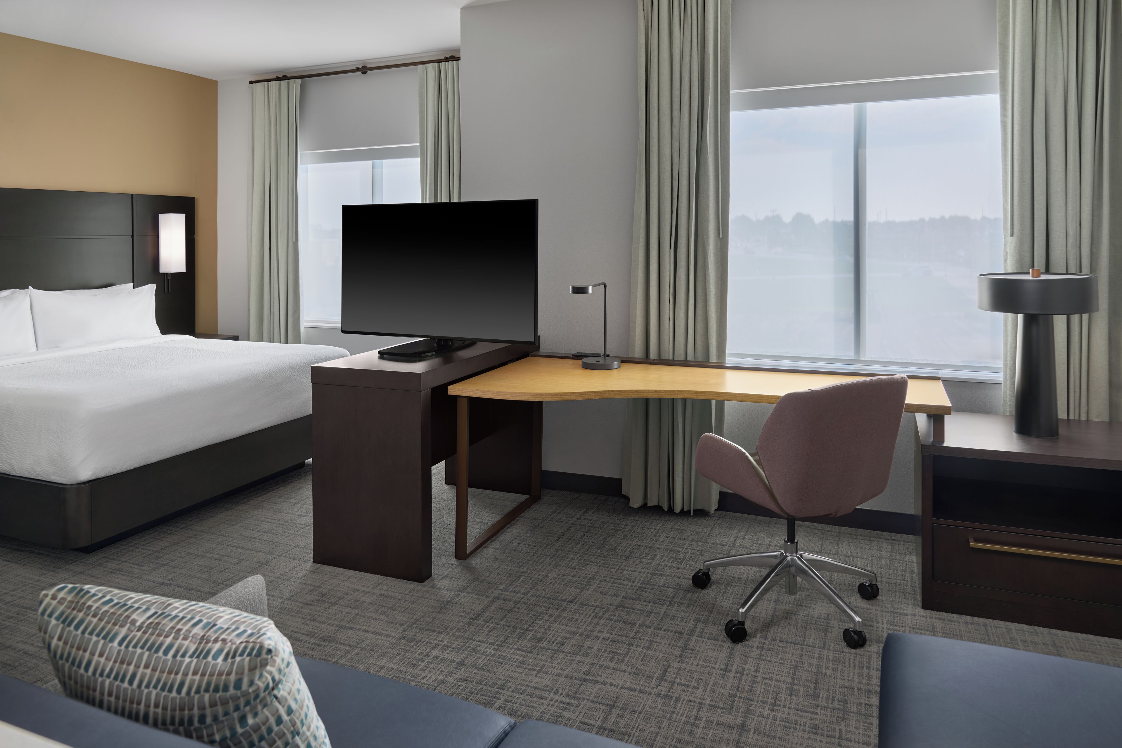 A hotel room with a bed, desk, chair, and a television.