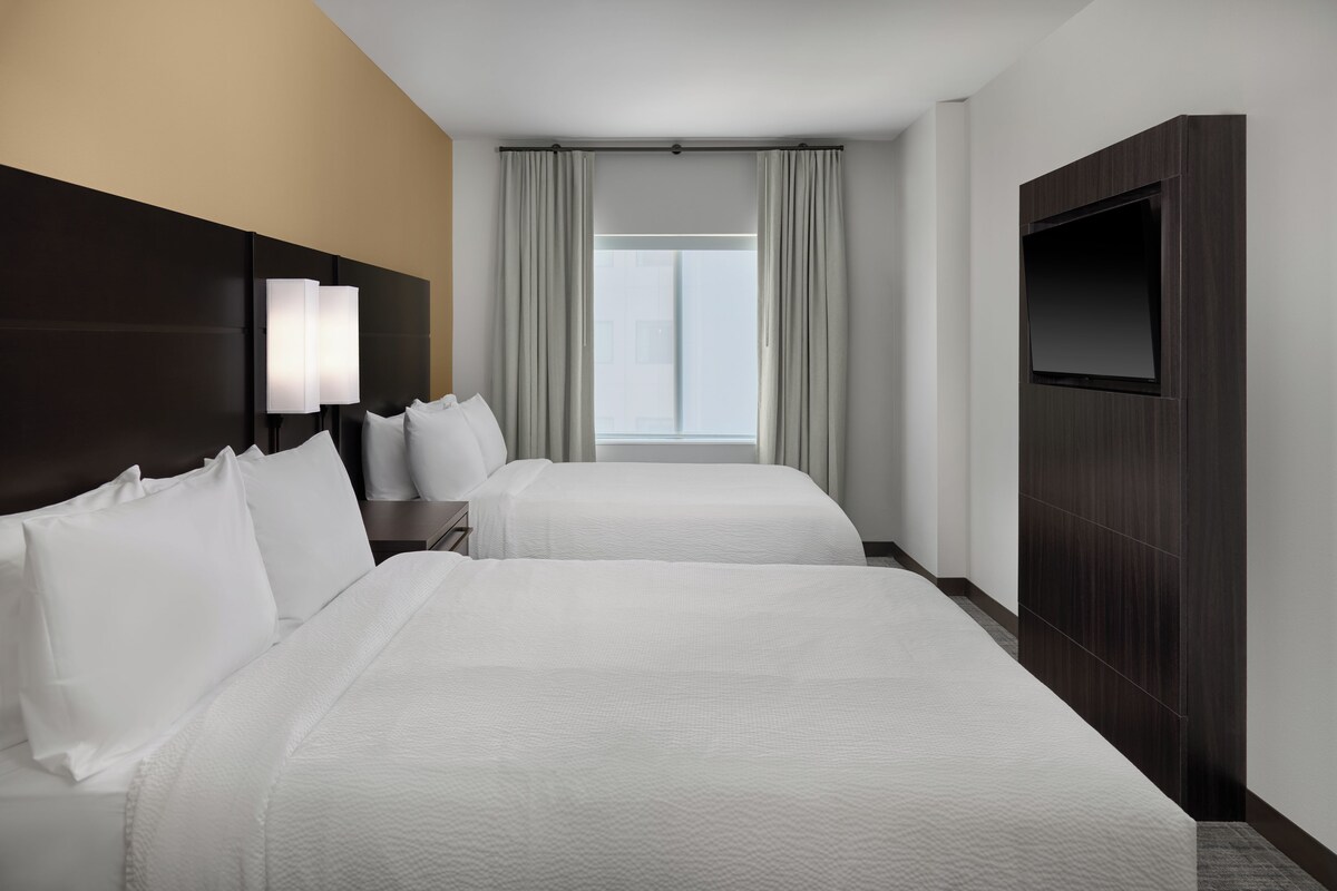 A hotel room with two beds, a TV, and a window with curtains.