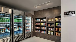 Un mercado bien iluminado con dispensadores de bebidas refrigeradas, estantes con bocadillos y un letrero que dice 'the market'.