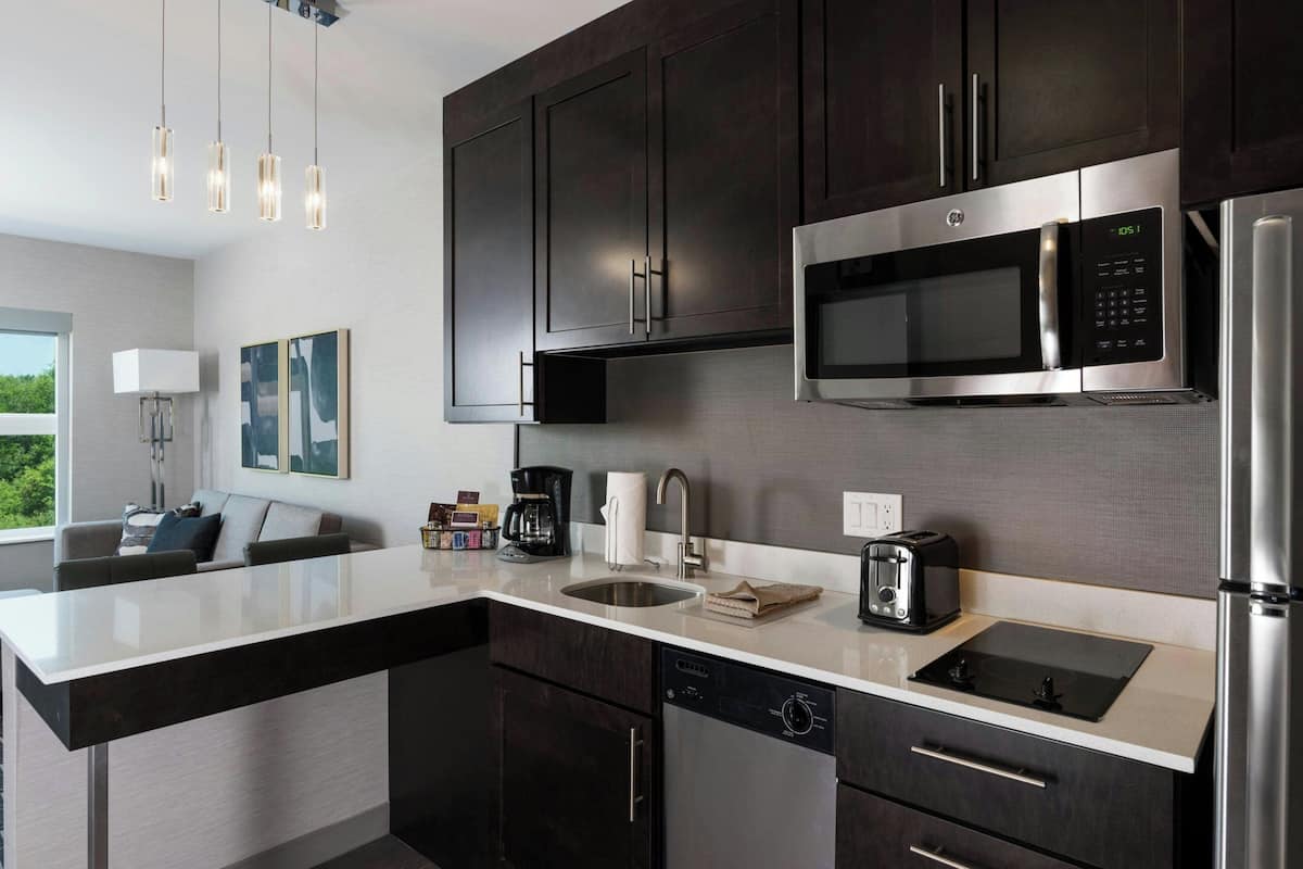 A modern kitchen with dark cabinets, stainless steel appliances, a built-in microwave, and a large island with a sink.