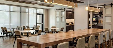 A spacious dining area with a long wooden table and multiple chairs, a kitchen area with dark wooden cabinets, and large windows allowing natural light.