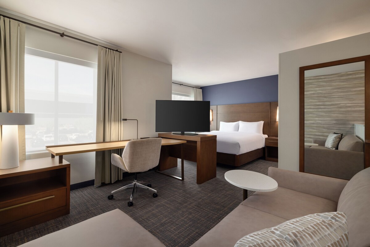 A hotel room with a desk, chair, bed, and a small round table.