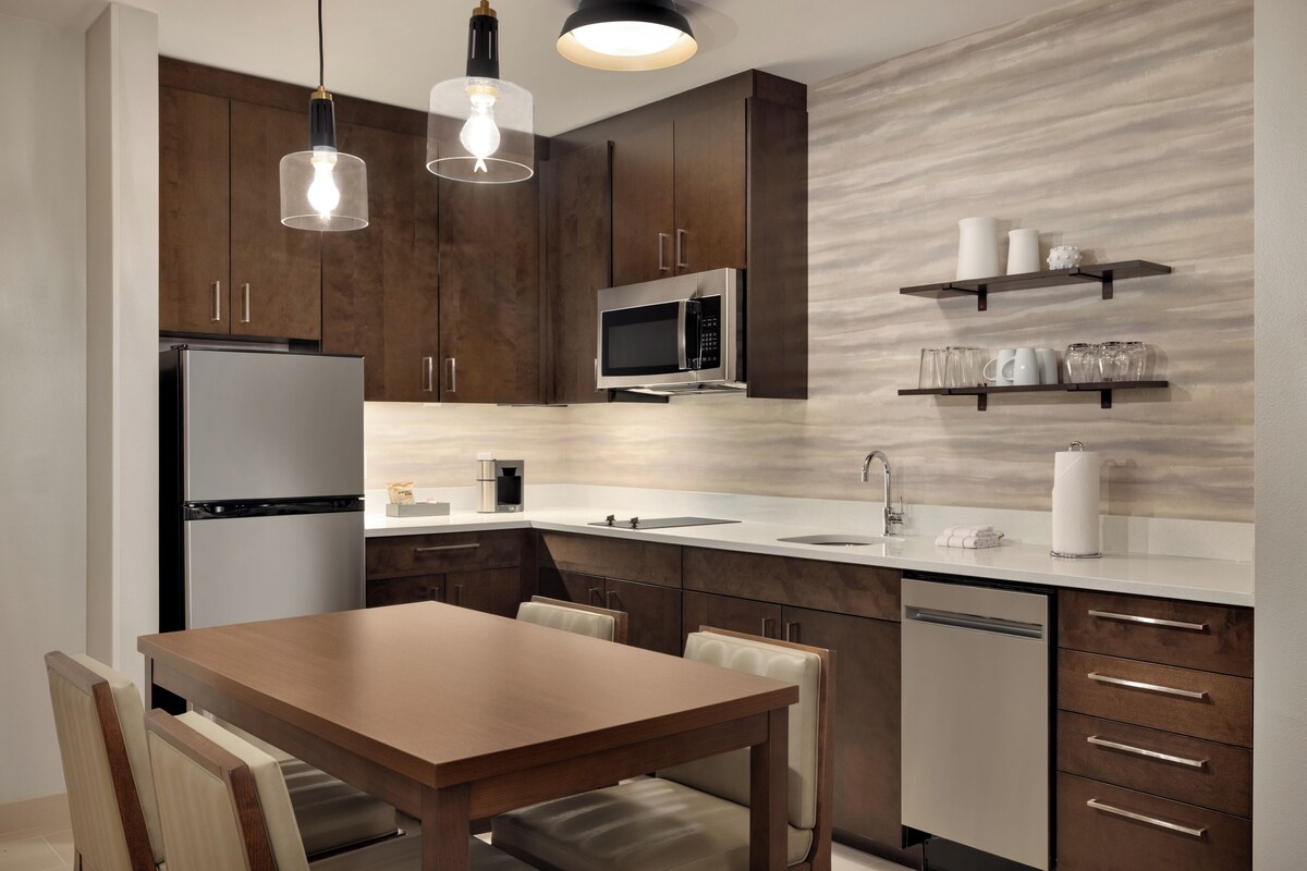A modern kitchen with stainless steel appliances, wooden cabinets, and a dining area with a table and chairs.