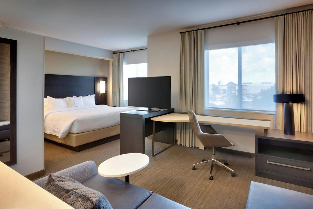 Habitación de hotel con cama, escritorio, silla y un amplio ventanal con cortinas.