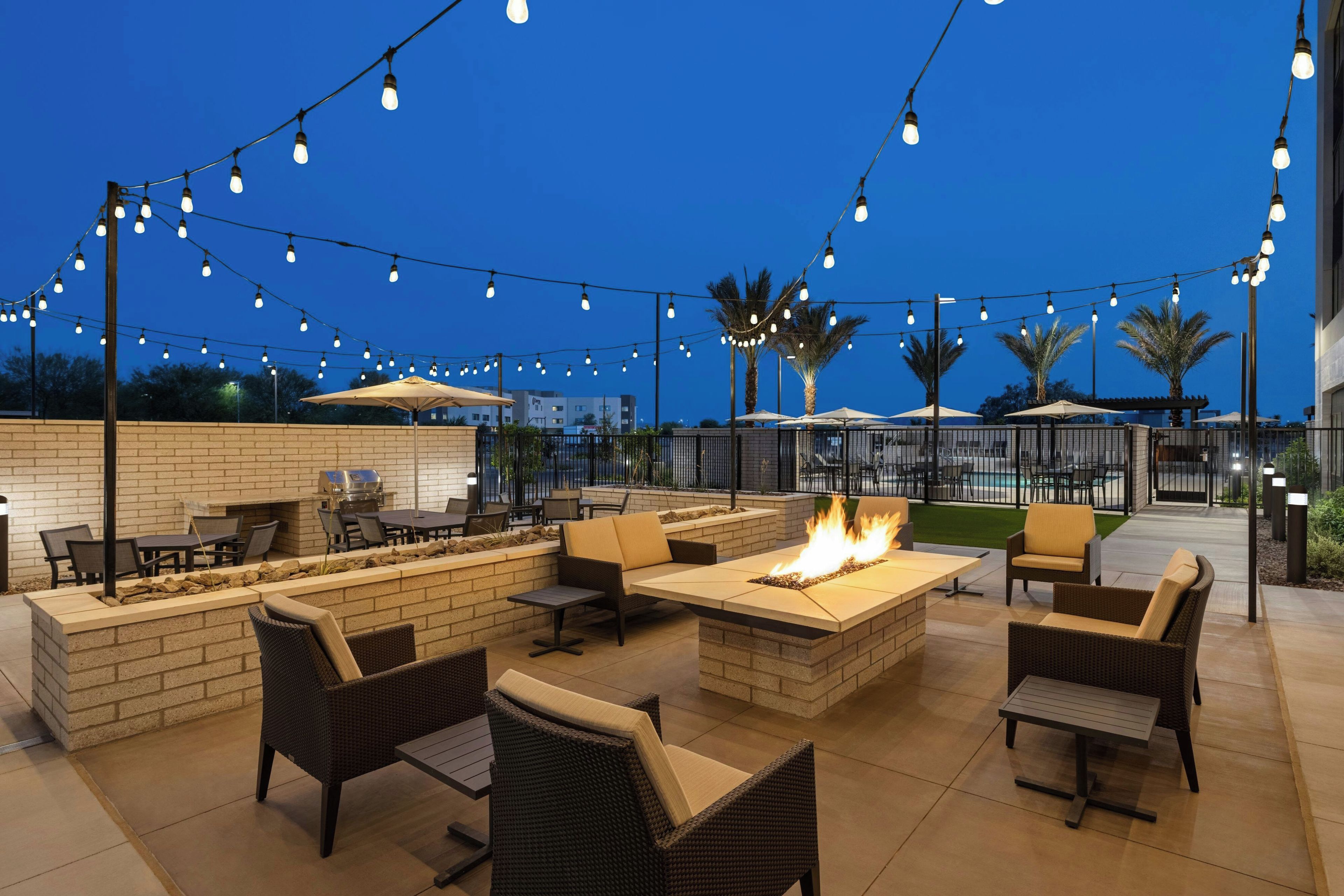 An outdoor patio with seating, a fire feature, and string lights against a clear sky.