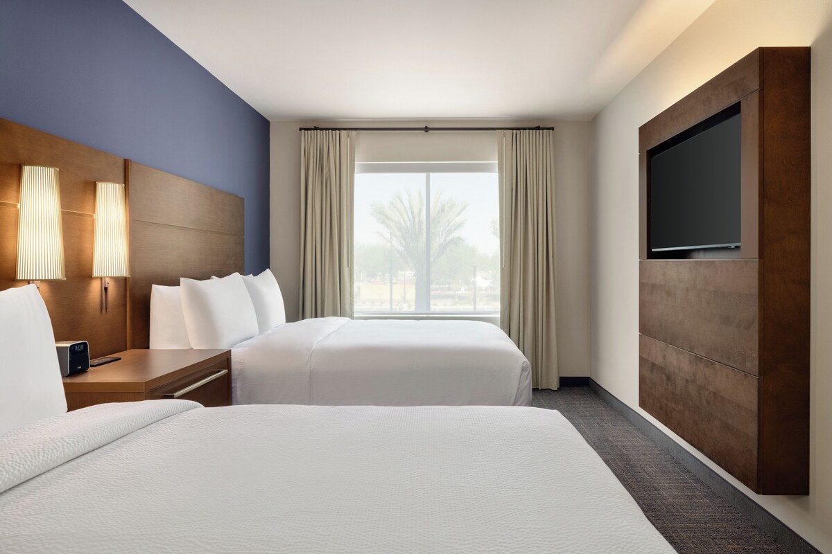A hotel room with two beds, a TV, a nightstand, and a window with curtains.