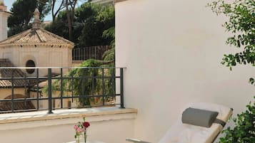 Ein sonnendurchfluteter Außenbereich mit Liegestuhl und kleinem Tisch, einer weißen Wand und Blick auf ein Gebäude mit der Aufschrift 'IN REPUBLIQUE'.