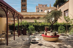 An outdoor patio area with seating arrangements, a pergola structure, and a view of a historic building with a bell tower. - Hotel Urbana, A Tribute Portfolio Hotel (Rome)