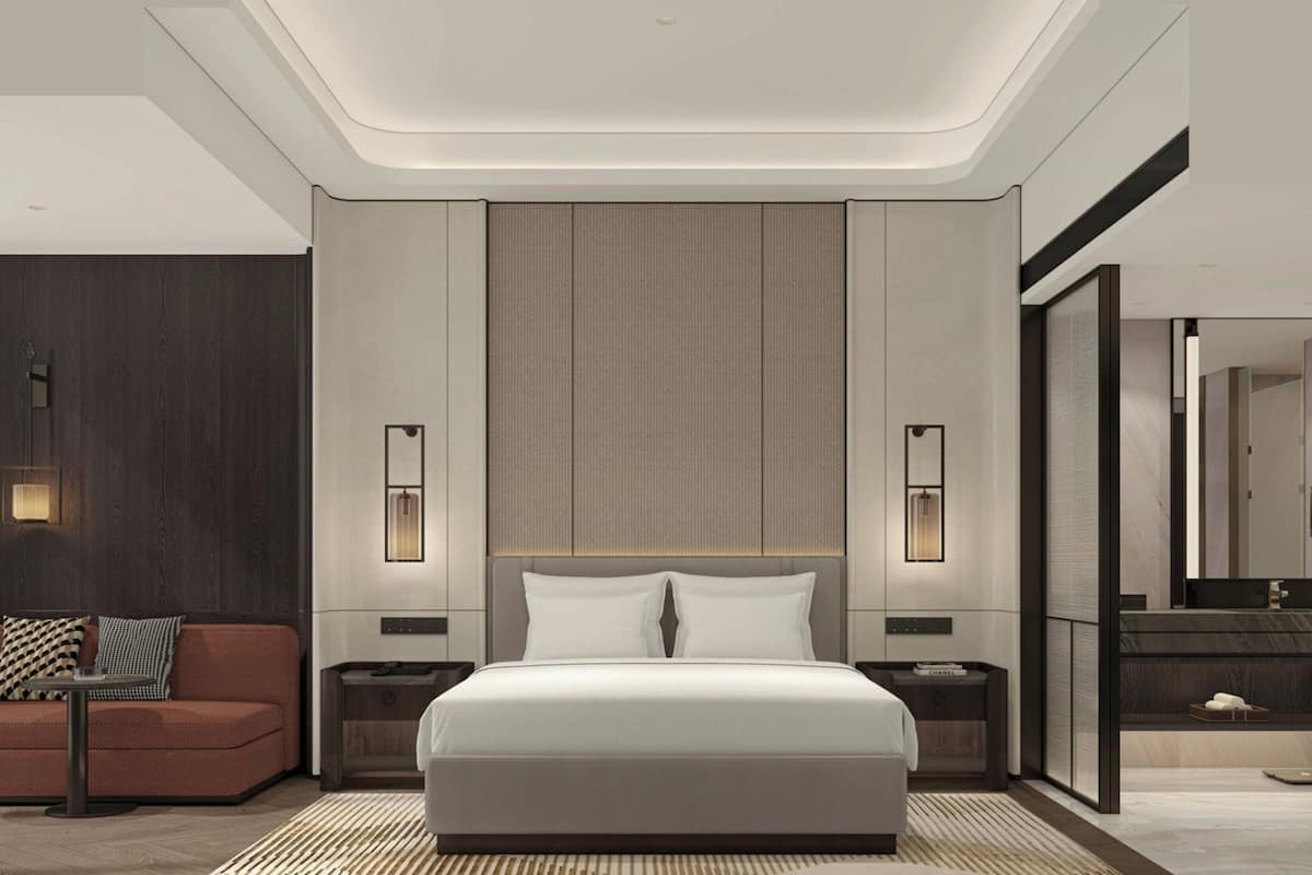 Una habitación de hotel moderna con una cama grande, un sofá, una mesita de noche, un espejo y una lámpara de pared.