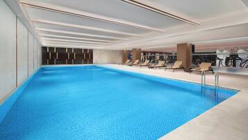 Una piscina interna moderna con superficie d'acqua blu trasparente, sedie a sdraio e attrezzature per l'esercizio fisico.