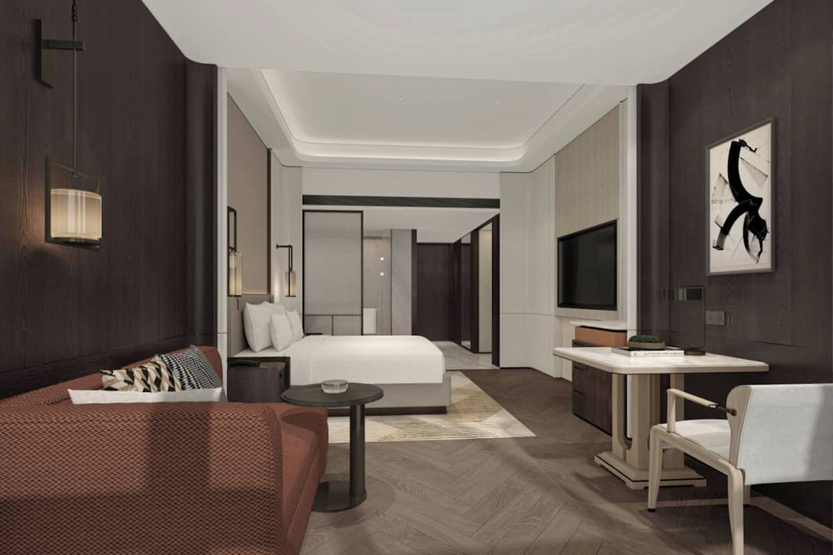 Habitación de hotel moderna con cama, mesita de noche, lámpara, televisión y un pequeño escritorio con una silla.