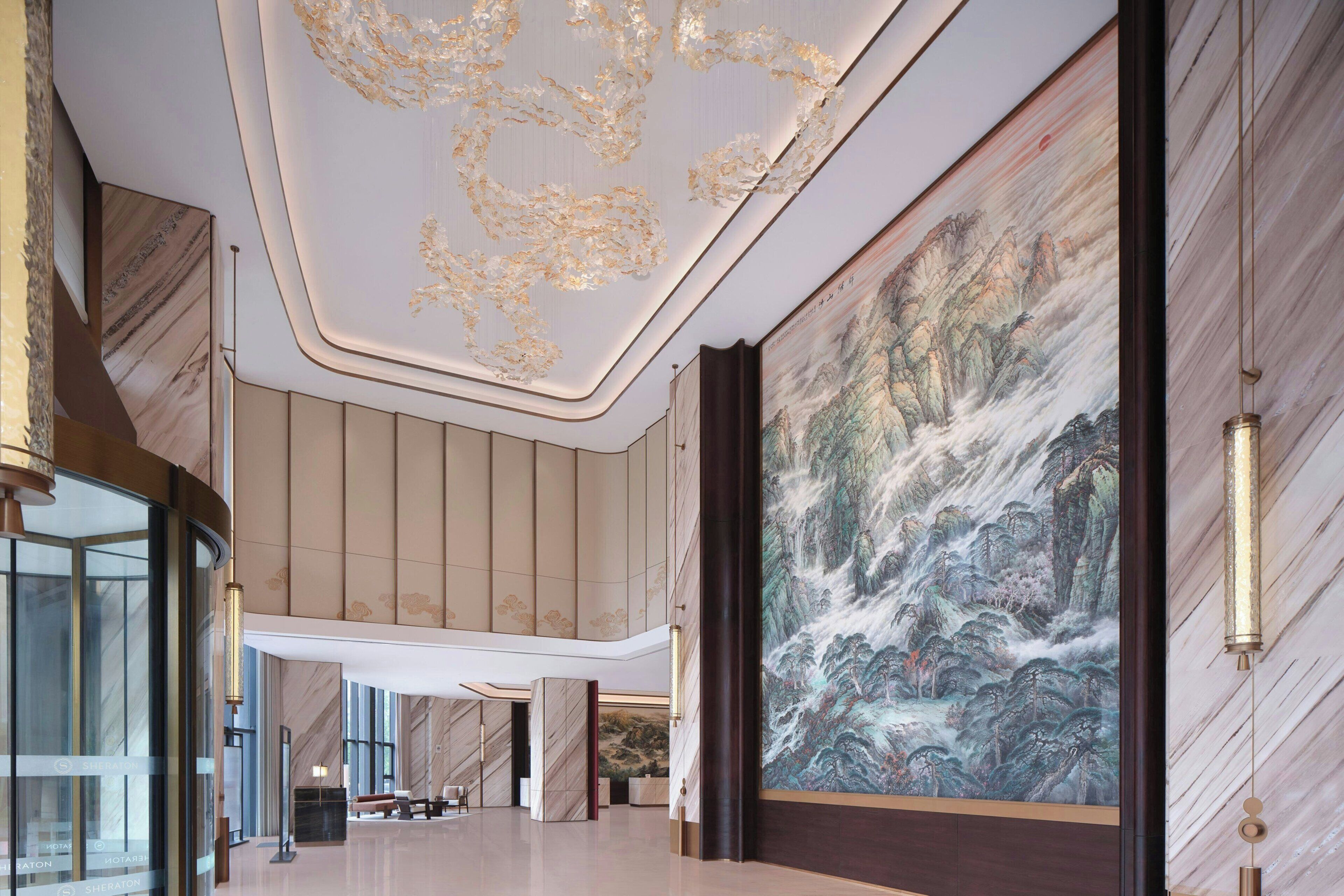 A spacious lobby with a large mural, a modern ceiling design, and a glass elevator.