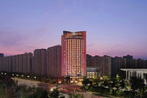 A high-rise hotel with a prominent logo on the top, surrounded by other buildings and a well-lit urban environment. - Sheraton Tengzhou (Zaozhuang)