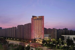 Un hotel de gran altura con un logotipo destacado en la parte superior, rodeado de otros edificios y un entorno urbano bien iluminado.