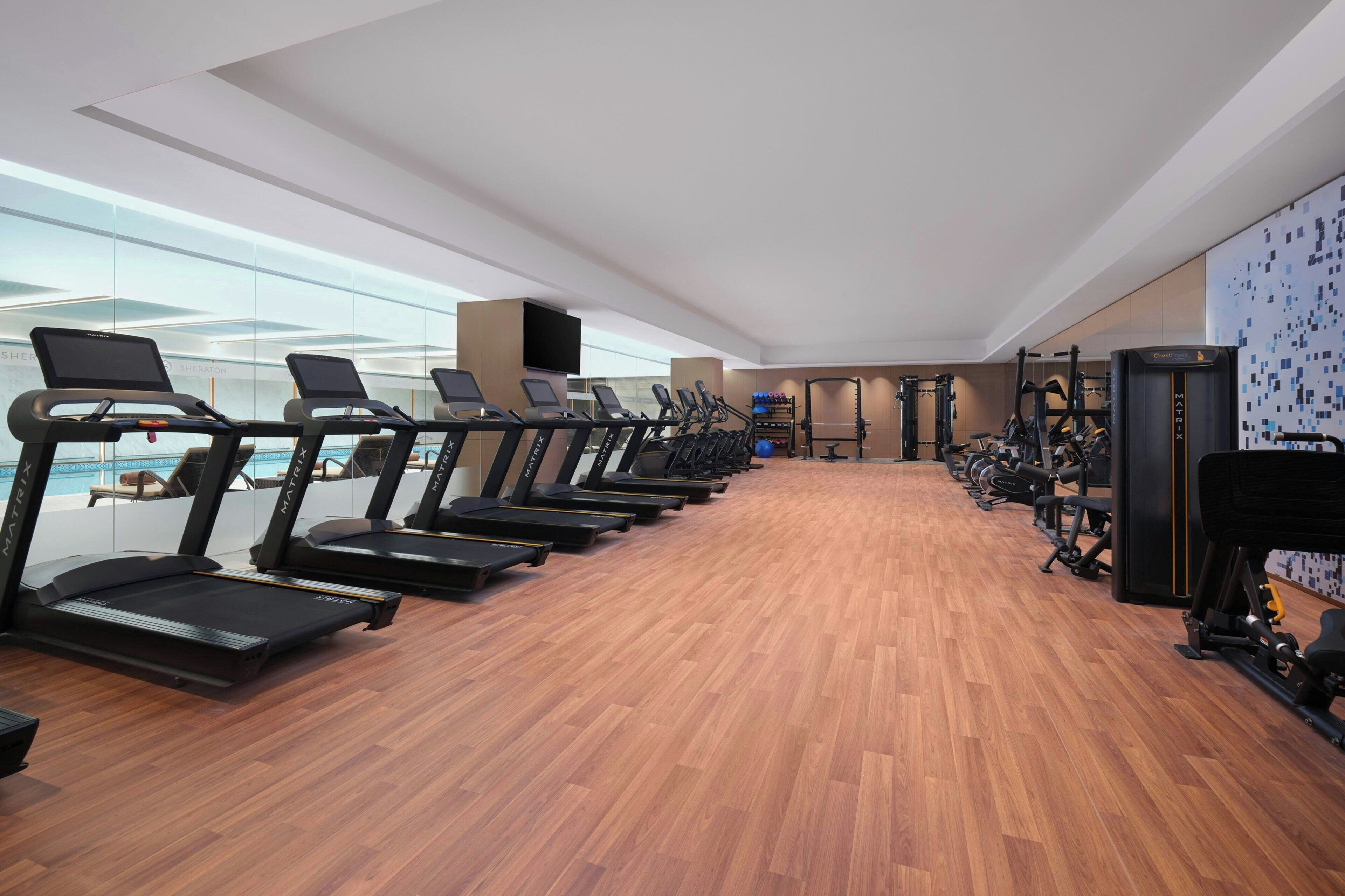 Un gimnasio con cintas de correr, máquinas de pesas y un amplio ventanal con vistas a una piscina.
