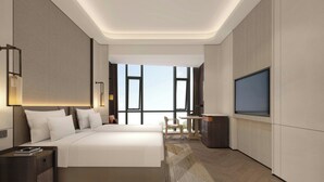Une chambre d’hôtel moderne dotée d’un grand lit, d’un bureau, d’une télévision et offrant une vue sur l’extérieur grâce à de grandes fenêtres.