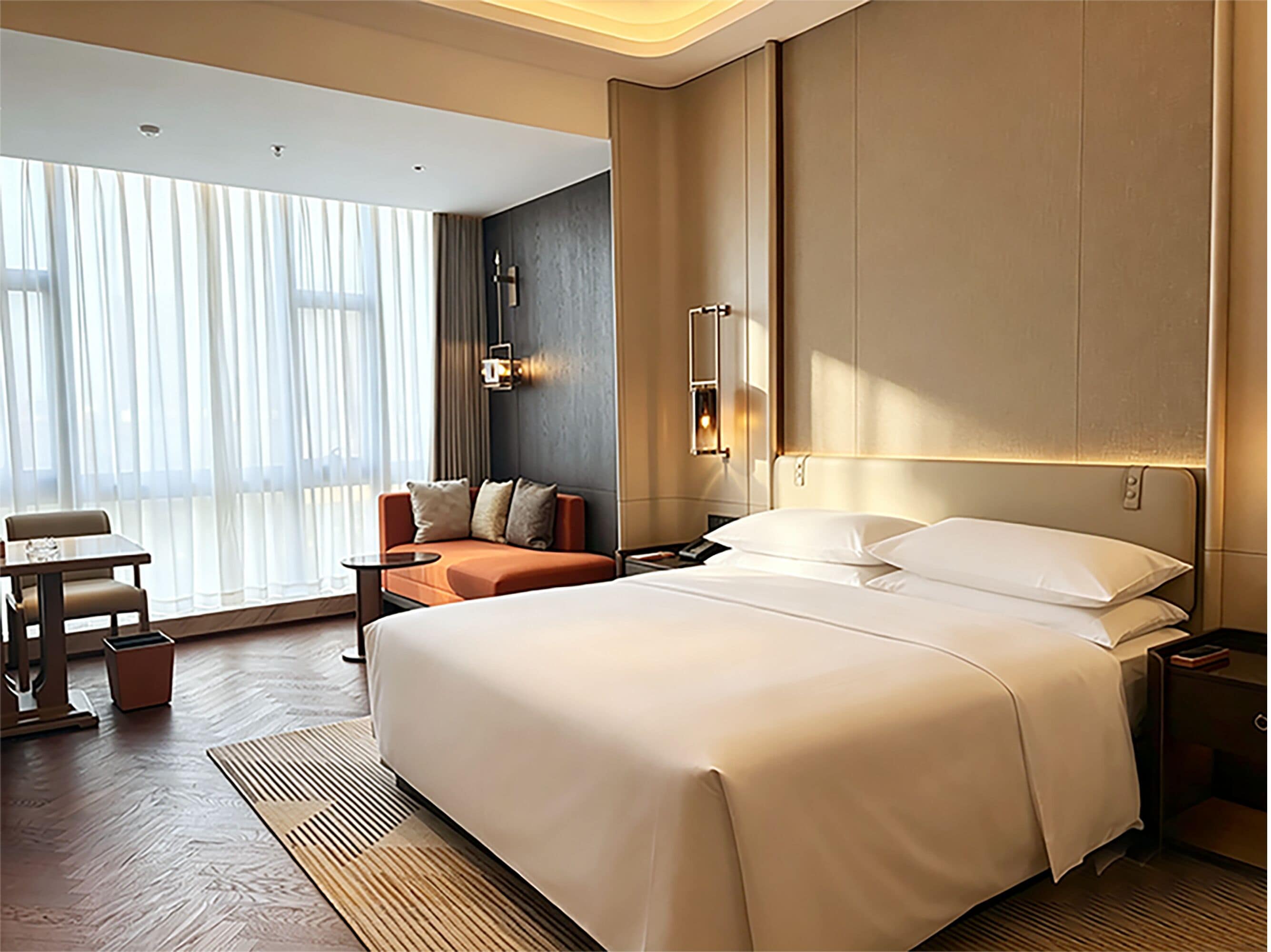 Habitació d'hotel amb un llit gran, un sofà, una taula de treball i una finestra gran amb cortines.