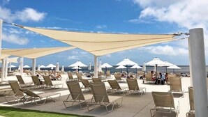 Eine Strandlounge mit Liegestühlen und Sonnenschirmen, ein klarer, blauer Himmel und das Meer im Hintergrund.