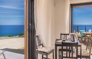 Een balkon met een tafel en stoelen, uitzicht op zee en een deur naar buiten.
