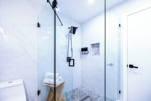Ein modernes Badezimmer mit einer Duschkabine aus Glas, Marmorwänden und einem gefliesten Boden.