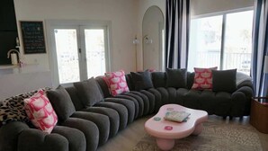 Un salon moderne avec un canapé d’angle, une table basse rose et un tapis à motifs.