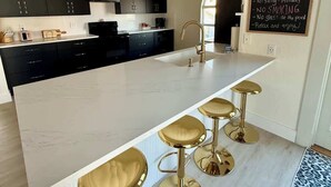 Une cuisine moderne dotée d’un îlot central, de tabourets de bar, de meubles de couleur sombre et d’un tableau noir sur lequel sont inscrites des règles.