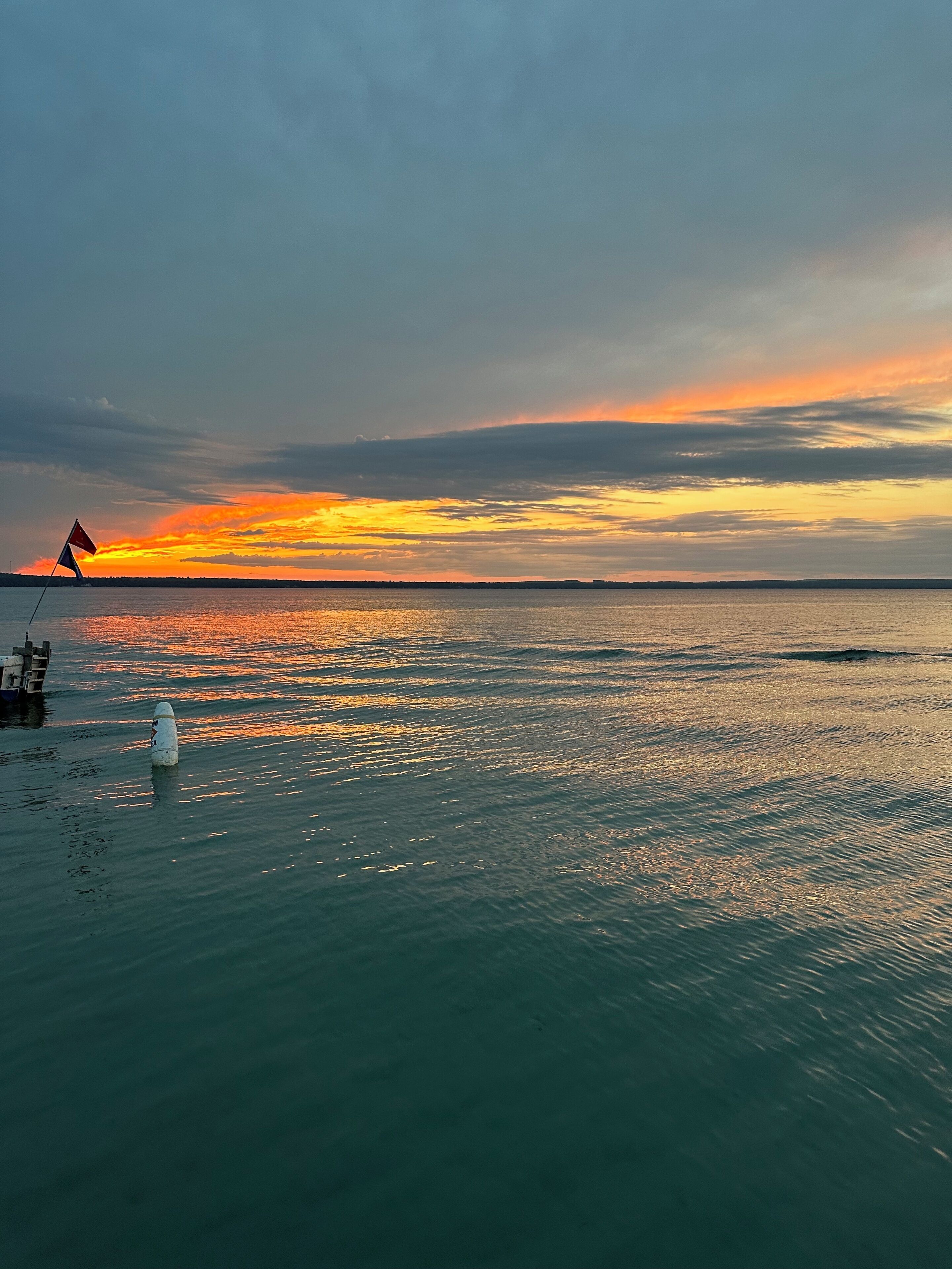 A calm body of water with a sunset, a flag, and a buoy.