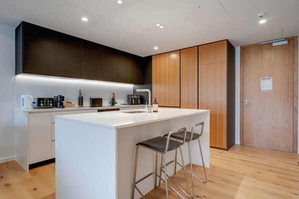 A modern kitchen with a central island, bar stools, wooden cabinets, and built-in appliances.