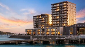 Un hotel modern amb diversos pisos, vistes al mar i un moll amb vaixells.