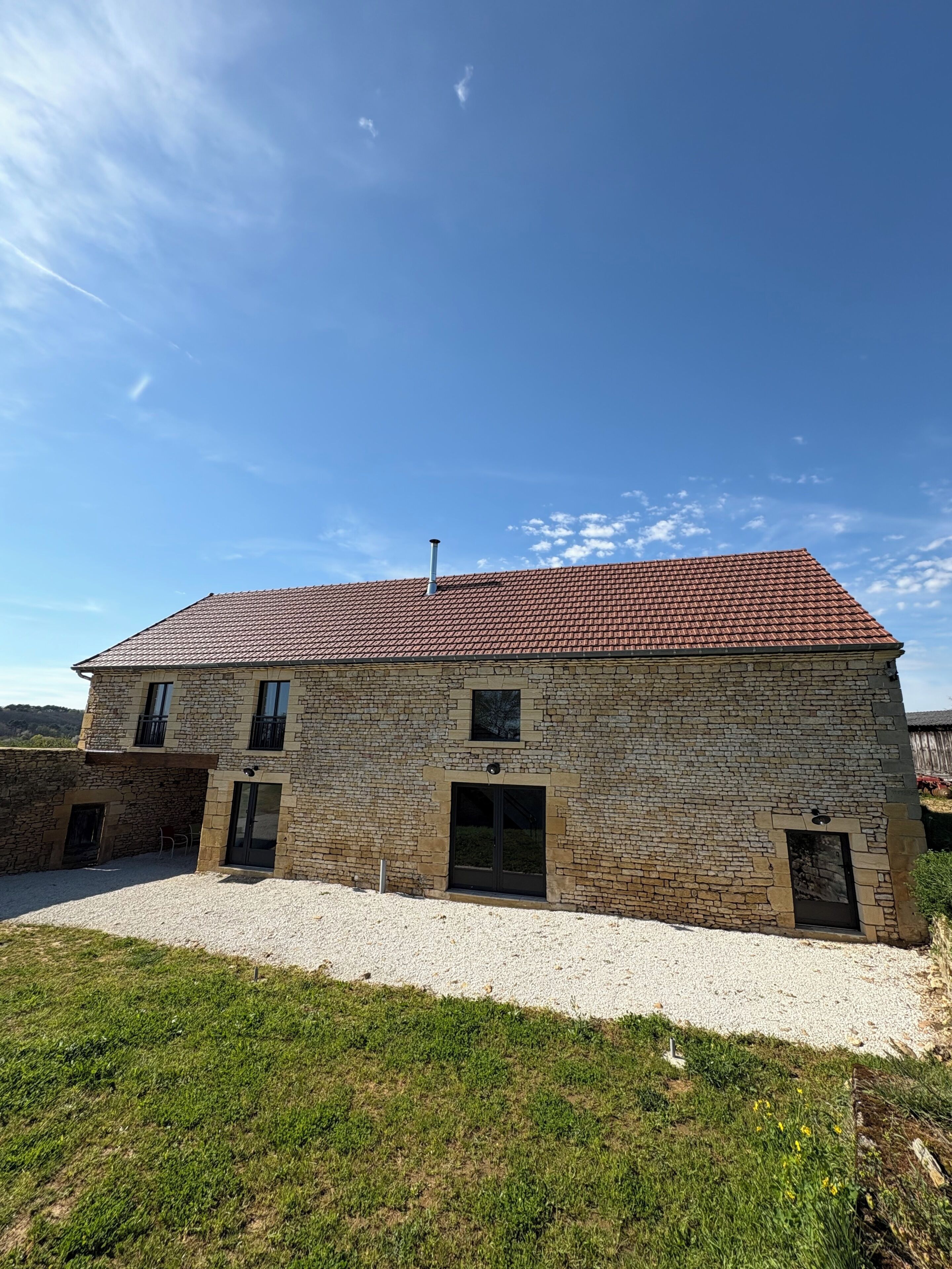A stone building with a red-tiled roof, a gravel driveway, and a grassy area in front.