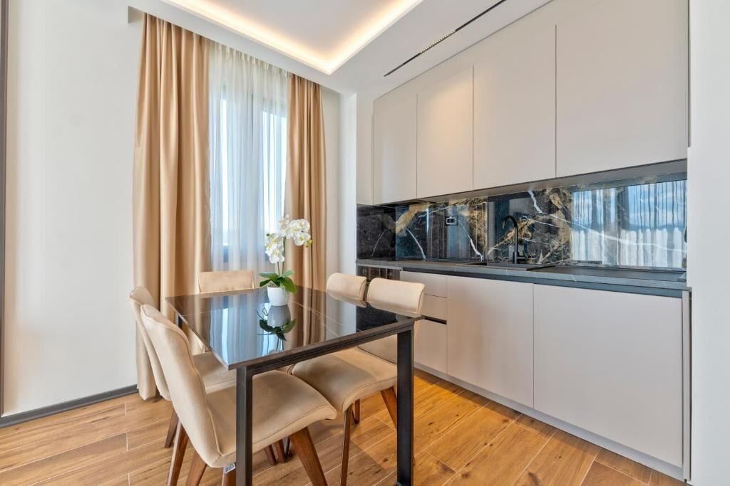 A modern kitchen with white cabinets, a marble backsplash, and a dining area with a glass table and chairs.