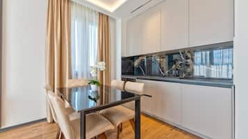 Una cocina moderna con gabinetes blancos, salpicadero de mármol y comedor con mesa y sillas de vidrio.